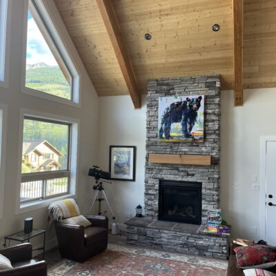 Zac's New Hiking Friend, original black bear cub painting by Verne Busby installed above a stone fireplace | Effusion Art Gallery in Invermere, BC