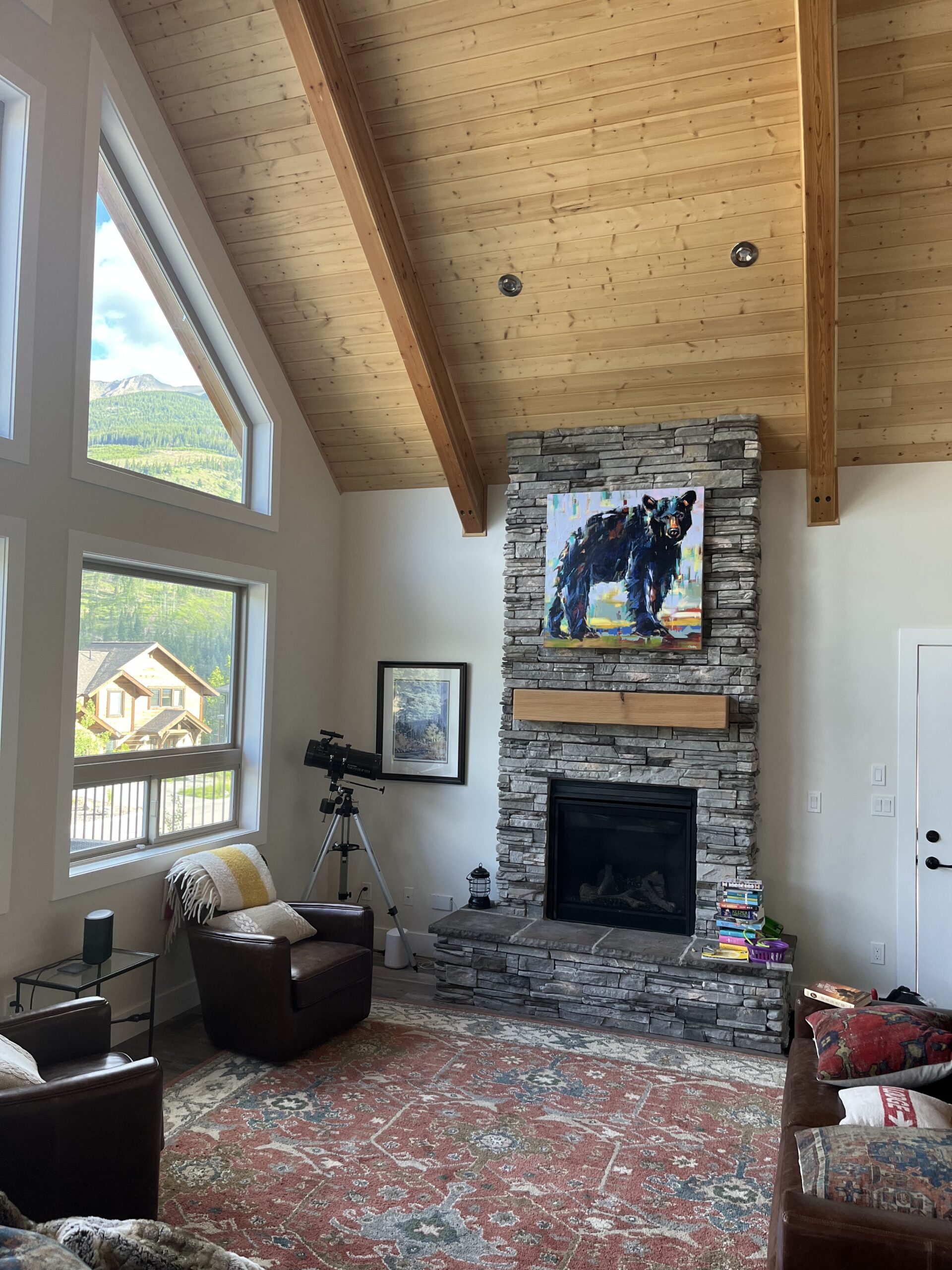 Cute black bear cub painting by Verne Busby installed above a rock fireplace in a cozy mountain home.