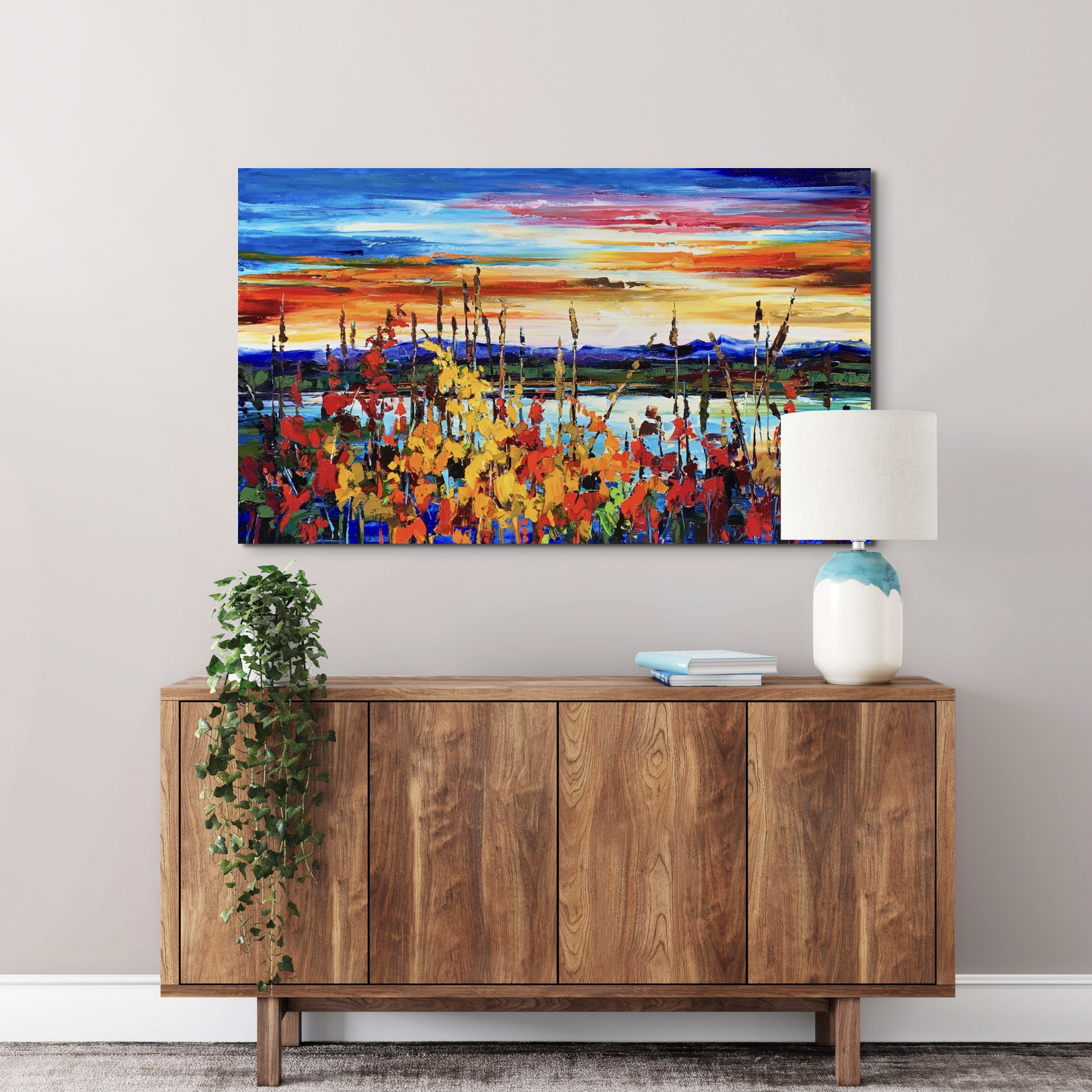 Kimberly Kiel oil painting of a vibrant sunset above a lake with colorful wildflowers in the foreground above a wooden mid-century modern cabinet.